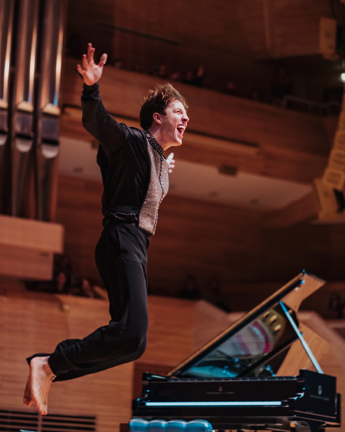 Stephen Ridley leaping into the air beside the piano mid-performance