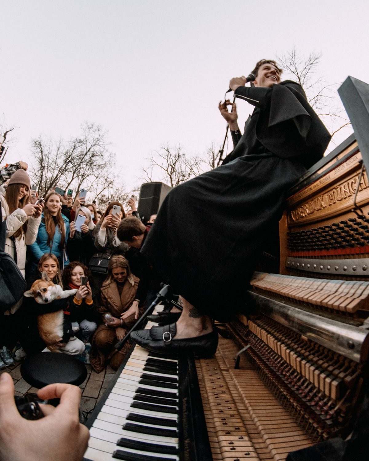 Stephen Ridley singing on top of a street piano surrounded by a huge crowd