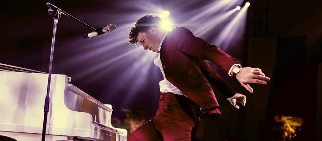 Stephen Ridley performing and singing at the piano under stage lights